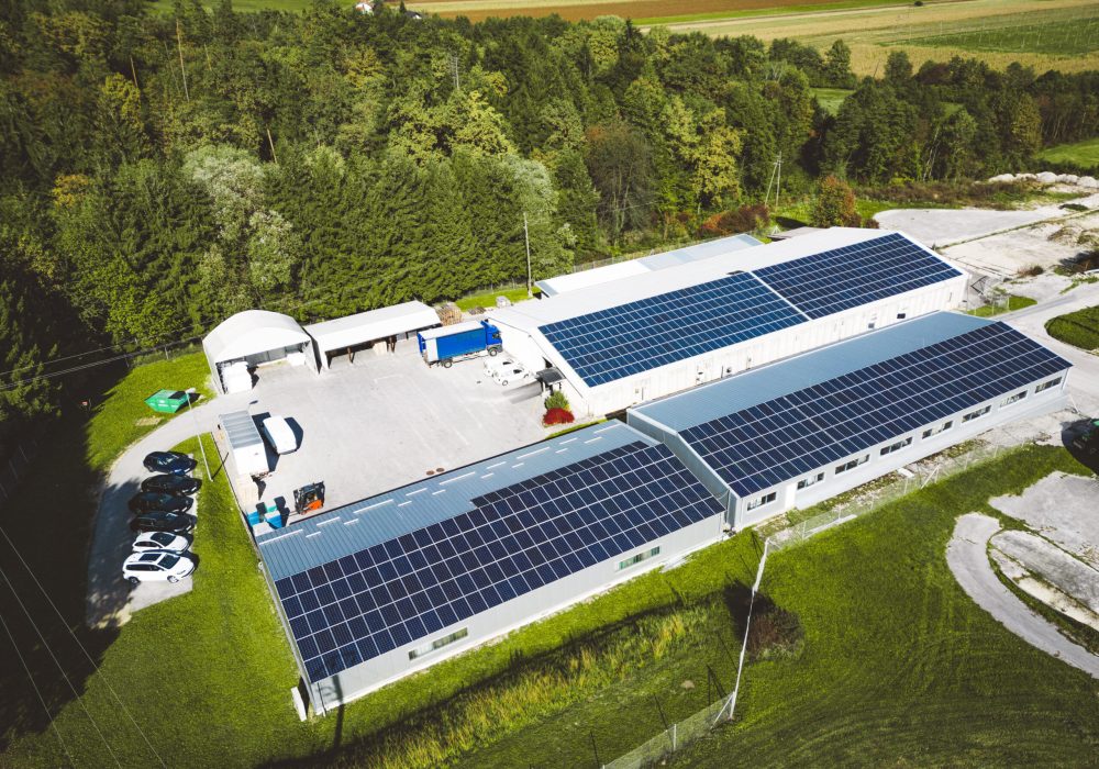Solar panels installed on a roof of a large industrial building or a warehouse. Industrial building in the country side of Slovenia with residential houses in the background. High quality photo
